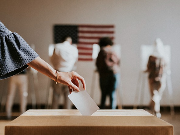 person placing vote in ballot box with US flag in background